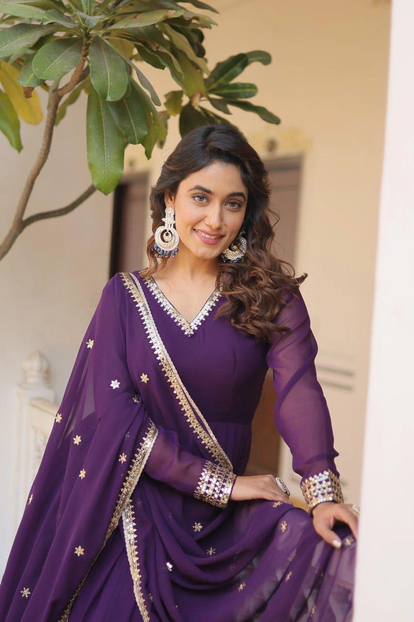 Woman in a purple saree with gold details standing outdoors.