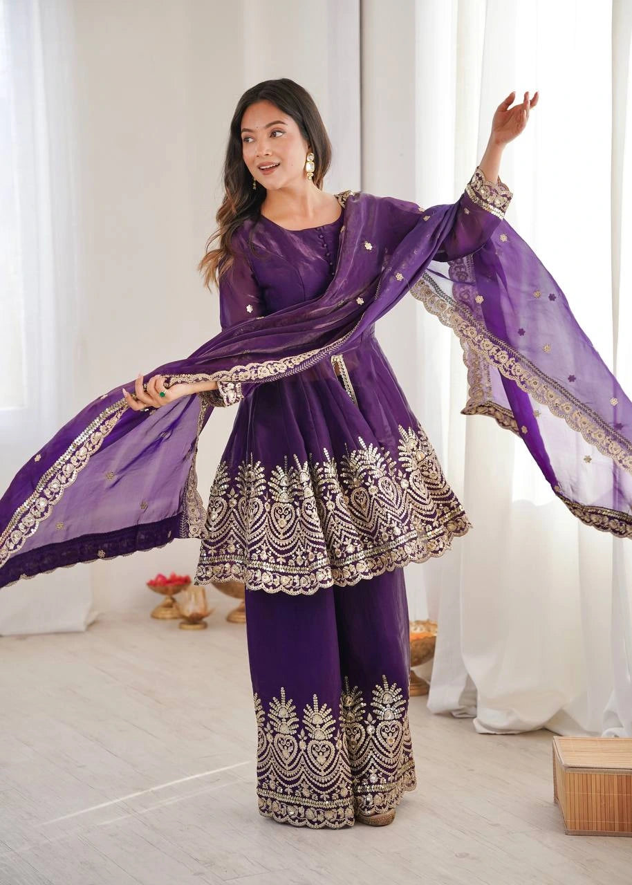 Woman in a purple traditional outfit with gold embroidery in a bright room.