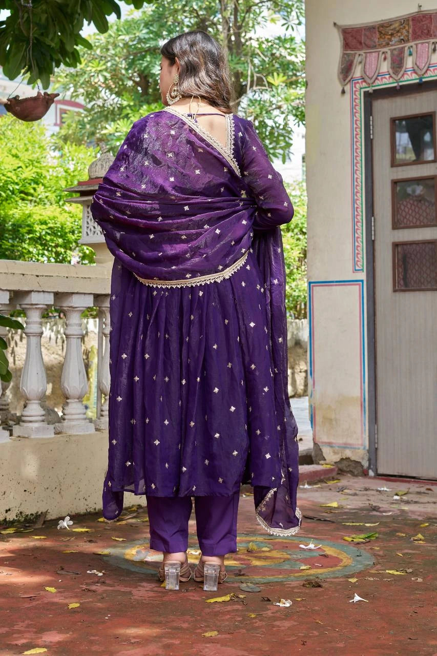 Woman in a purple traditional outfit standing outdoors near a building.