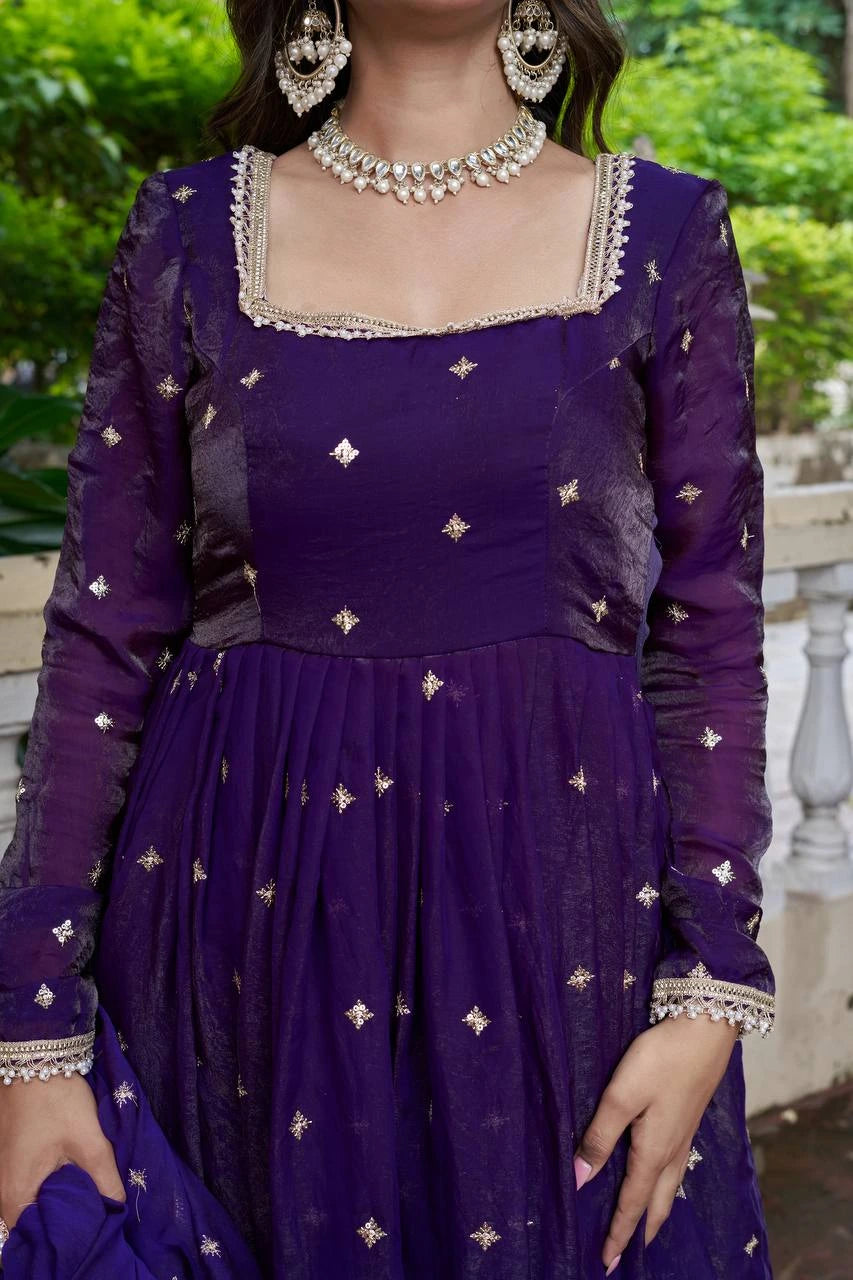 Purple traditional outfit with intricate designs and jewelry against a blurred green background