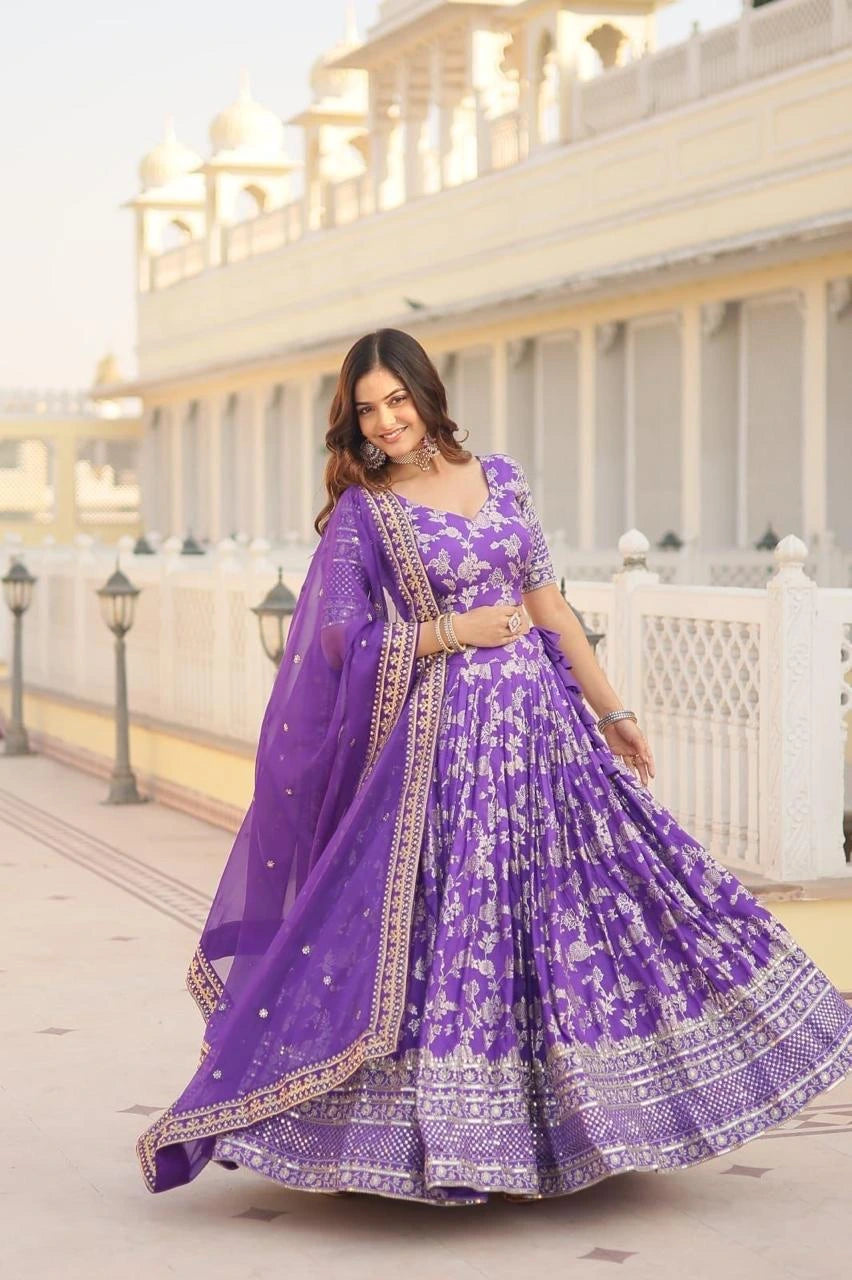 Woman in a purple traditional outfit standing in front of a white building.