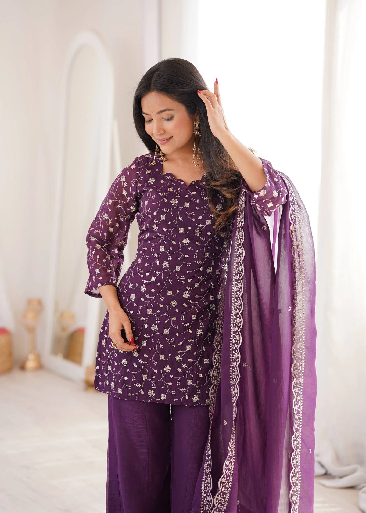 Woman wearing a purple traditional outfit with a matching dupatta in a well-lit room.