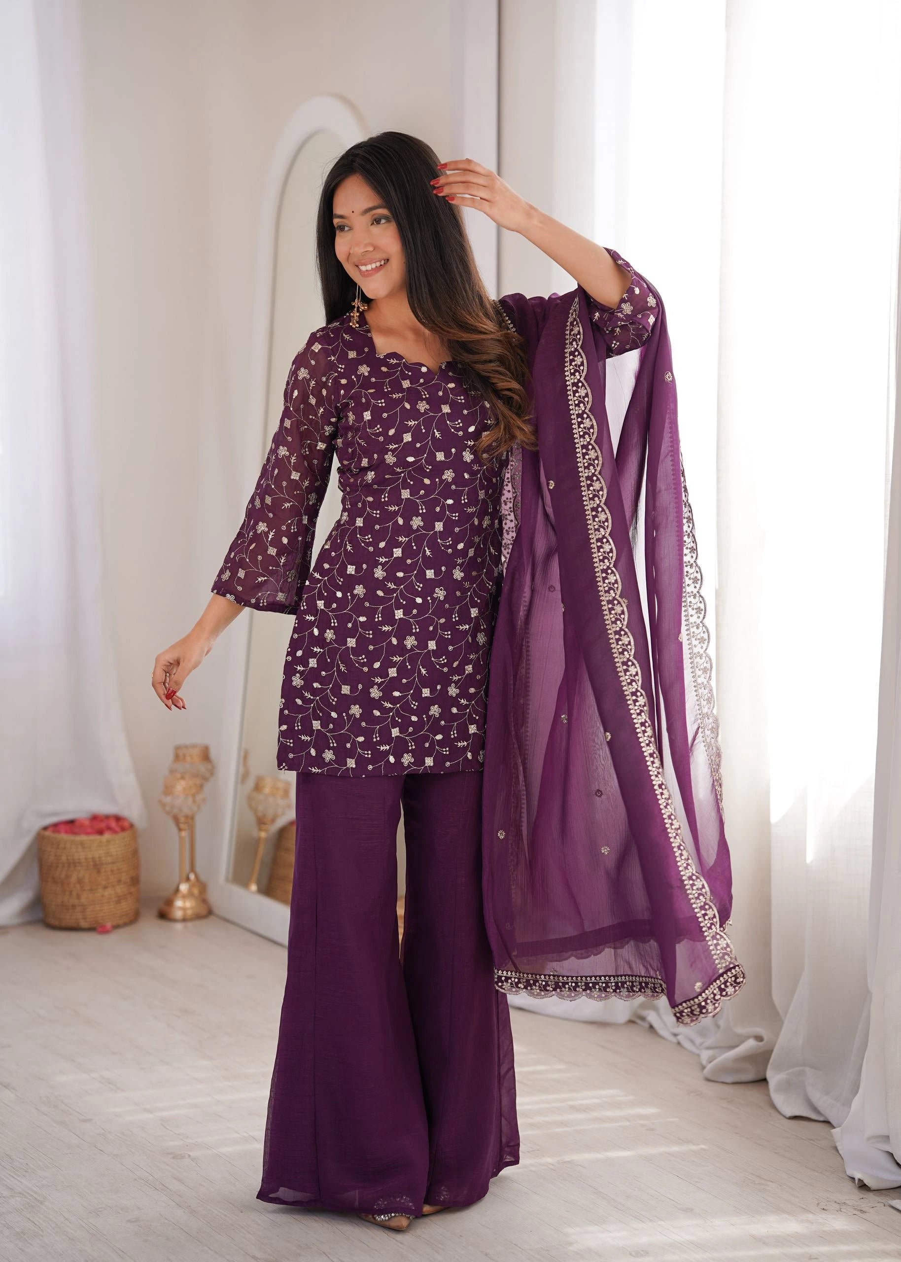 Woman in a purple traditional outfit with a matching dupatta in a bright room.