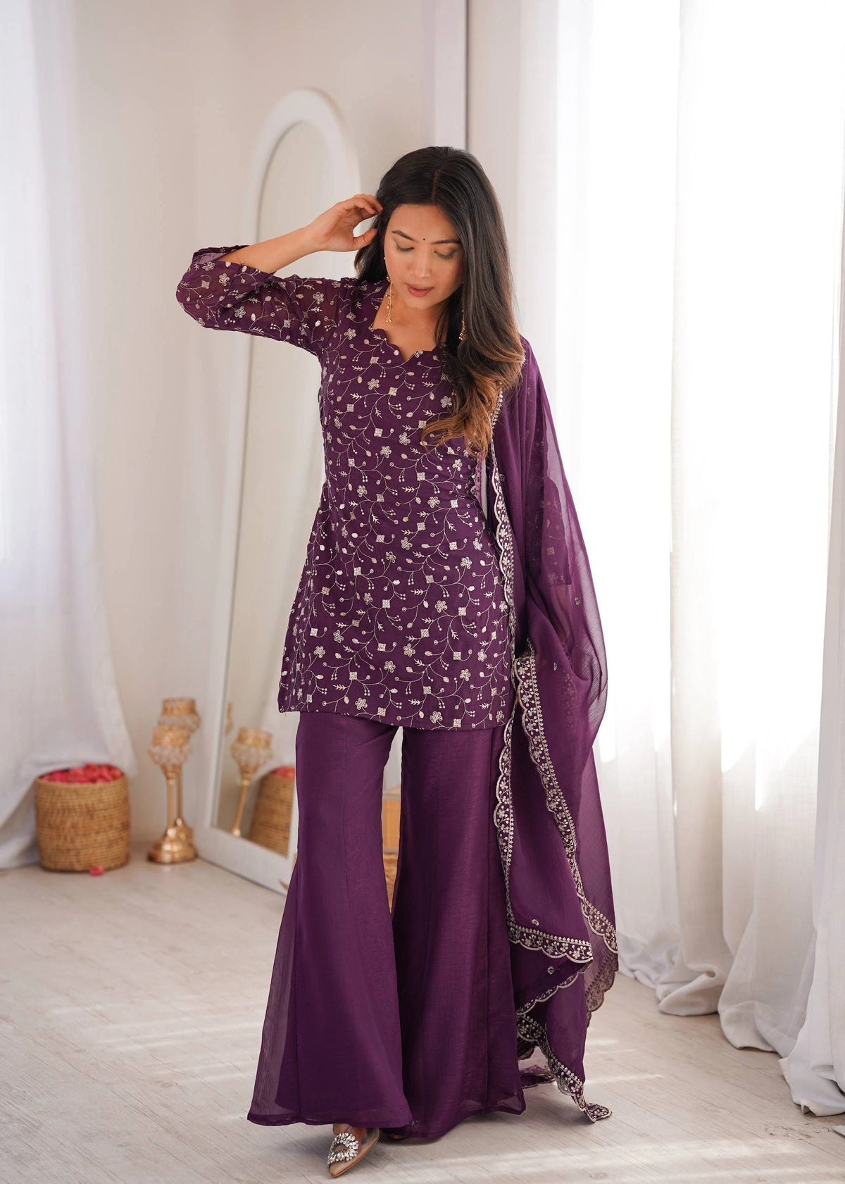 Woman in a purple traditional outfit with a matching dupatta in a bright room.