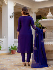 Woman in a purple traditional outfit standing in an elegant indoor setting with a fountain.