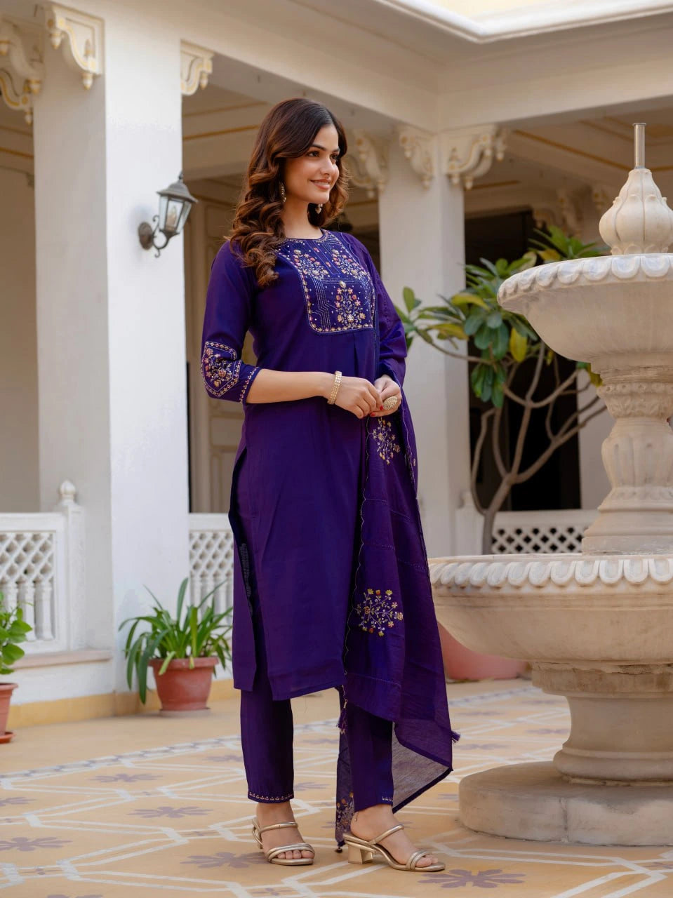 Woman in a purple traditional outfit standing in an elegant outdoor setting.