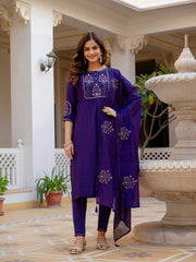 Woman in a purple traditional outfit standing in an outdoor setting with decorative elements.