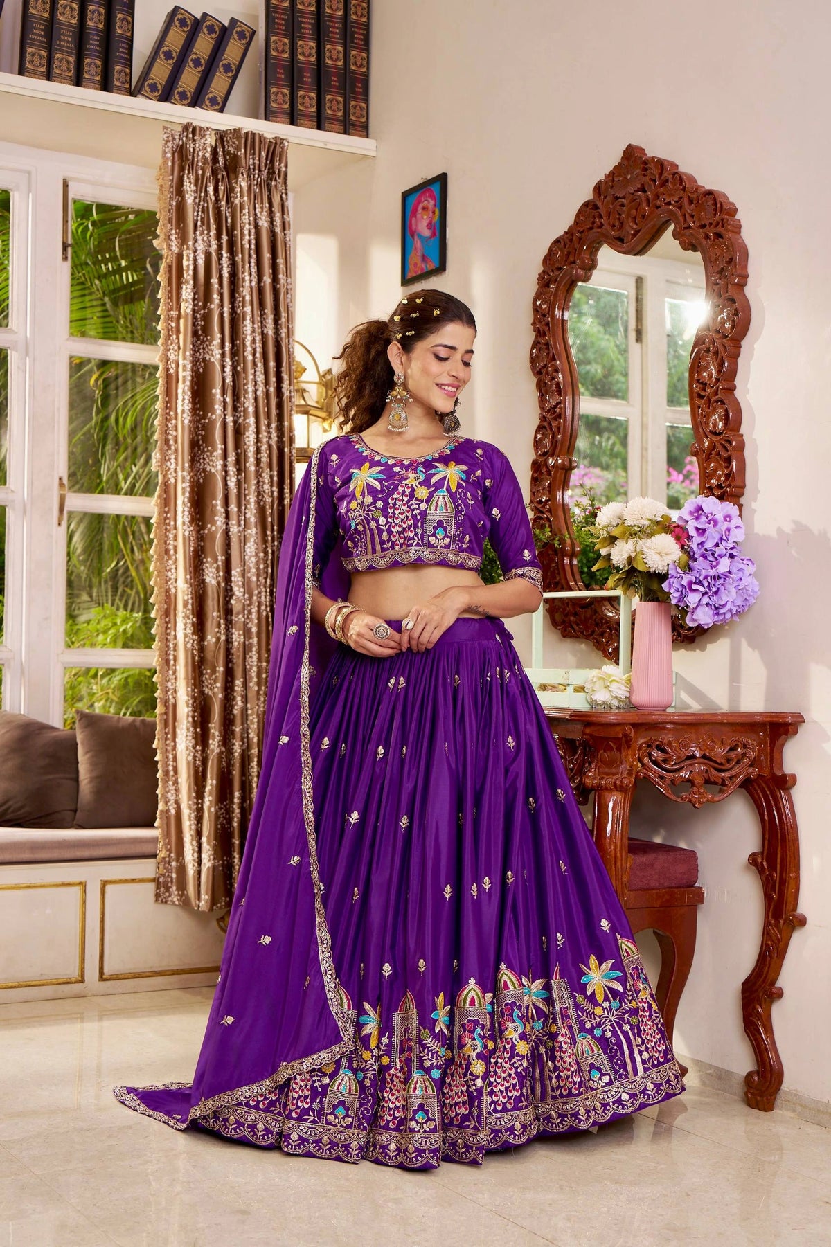 Woman in a purple embroidered traditional outfit standing in a room with decor elements.