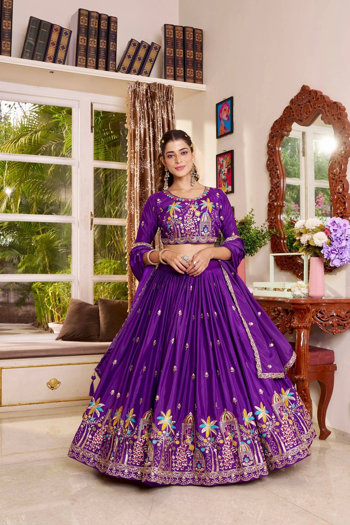 Woman in a purple embroidered traditional outfit standing in a room with decor elements.