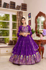 Woman in a purple embroidered traditional outfit standing in a room with decor elements.