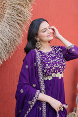 Woman wearing a purple traditional outfit with gold embroidery against a red wall.