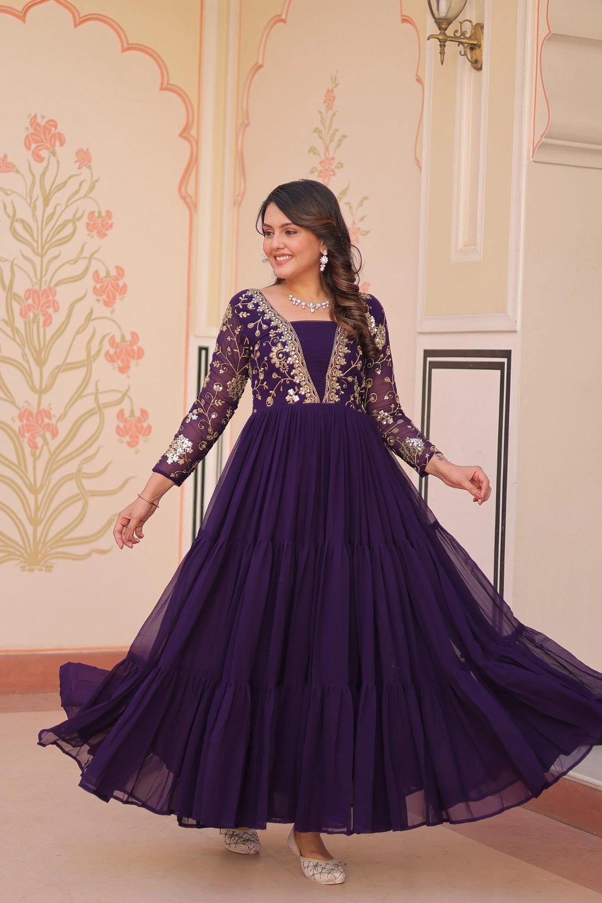 Woman wearing a purple gown with floral embroidery in an indoor setting.
