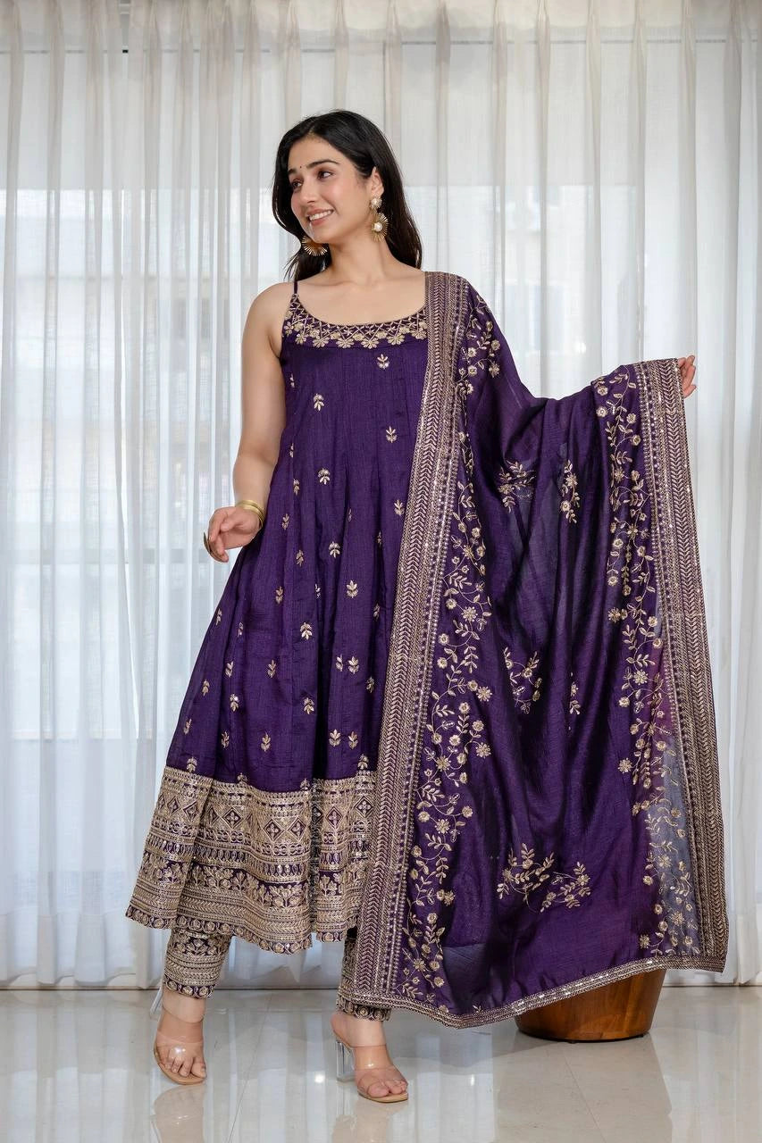 Woman wearing a purple traditional outfit with a matching dupatta against a white curtain background