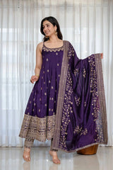 Woman wearing a purple traditional outfit with a matching dupatta against a white curtain background