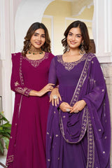 A medium shot of two women posing together. One wears a magenta Anarkali and the other a deep purple one. Both suits feature intricate gold zari embroidery around the scoop neckline and sequin-bordered dupattas.