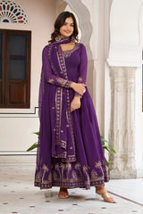 The woman stands centered in the frame, wearing the purple ensemble. The gold embroidery at the hemline is prominently displayed against the white marble floor.