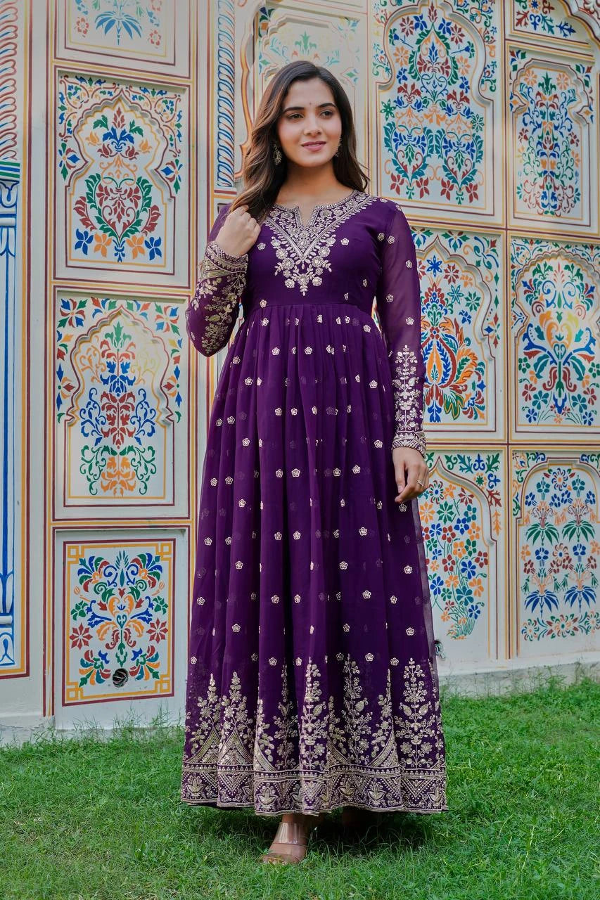 Woman in a purple dress with white embroidery standing in front of a colorful wall.