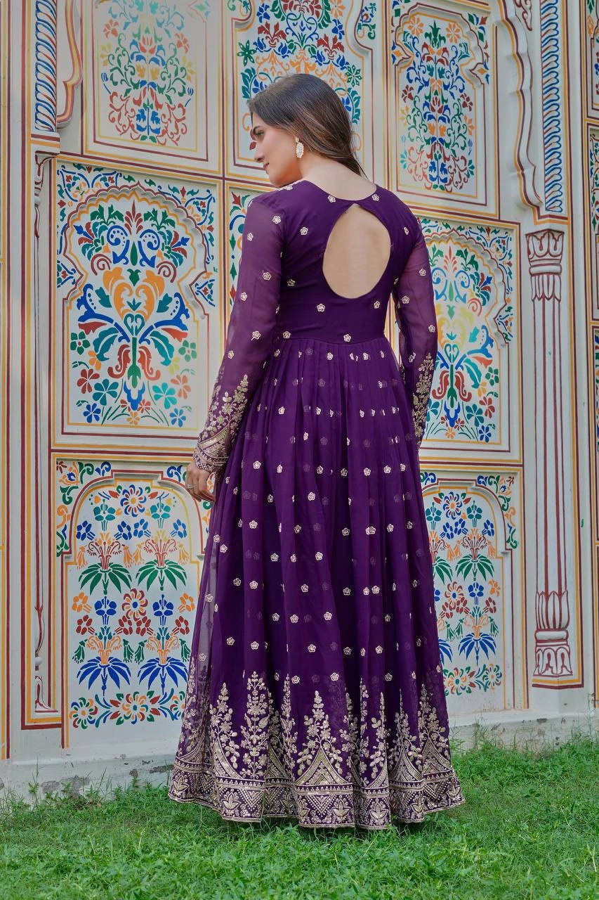 Woman in a purple dress with cut-out back standing in front of a colorful patterned wall.