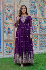 Woman in a purple dress with white embroidery standing in front of a colorful wall.