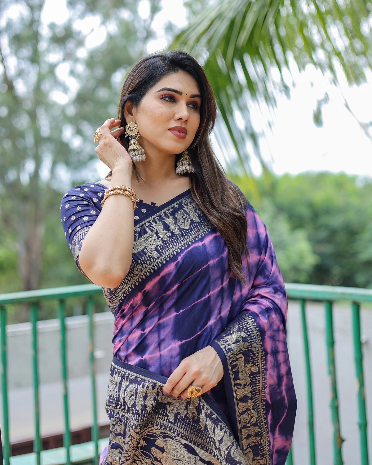 Woman wearing a purple saree with a green outdoor background