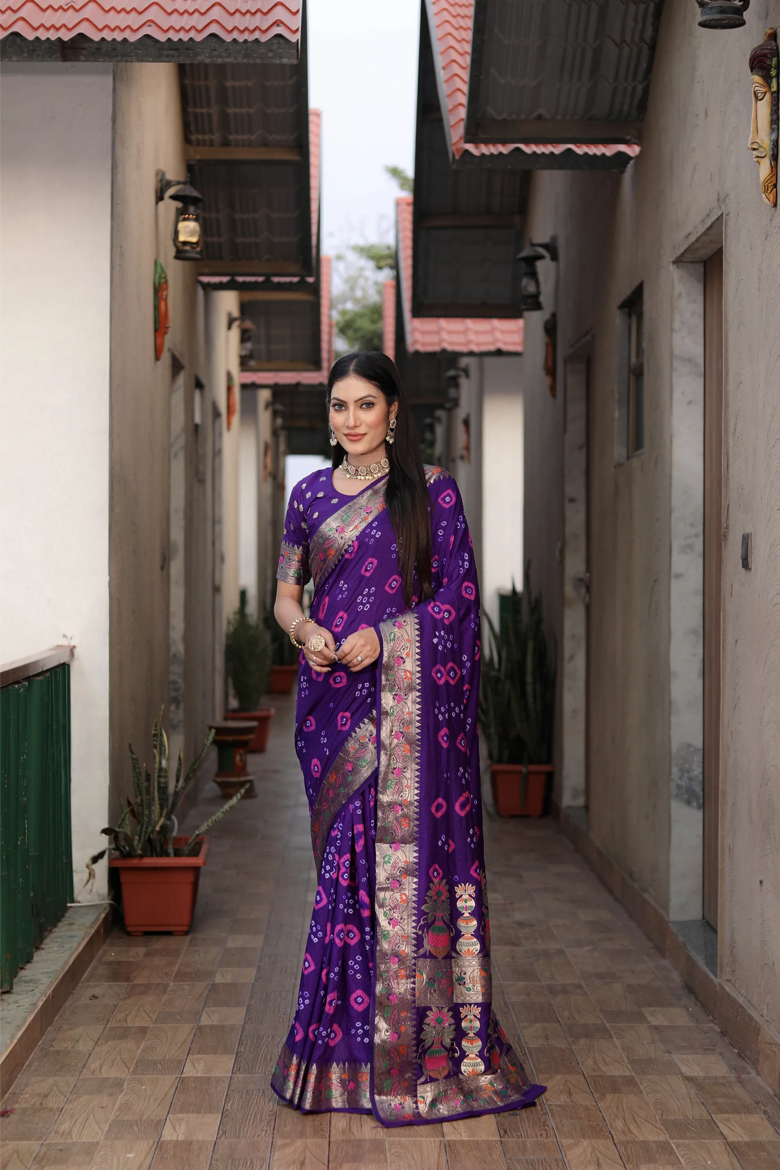 Woman in a purple saree standing in a narrow alleyway.