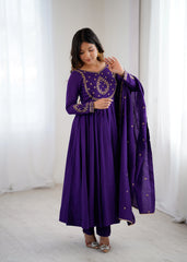 Woman wearing a purple traditional outfit with gold embroidery in a white room.