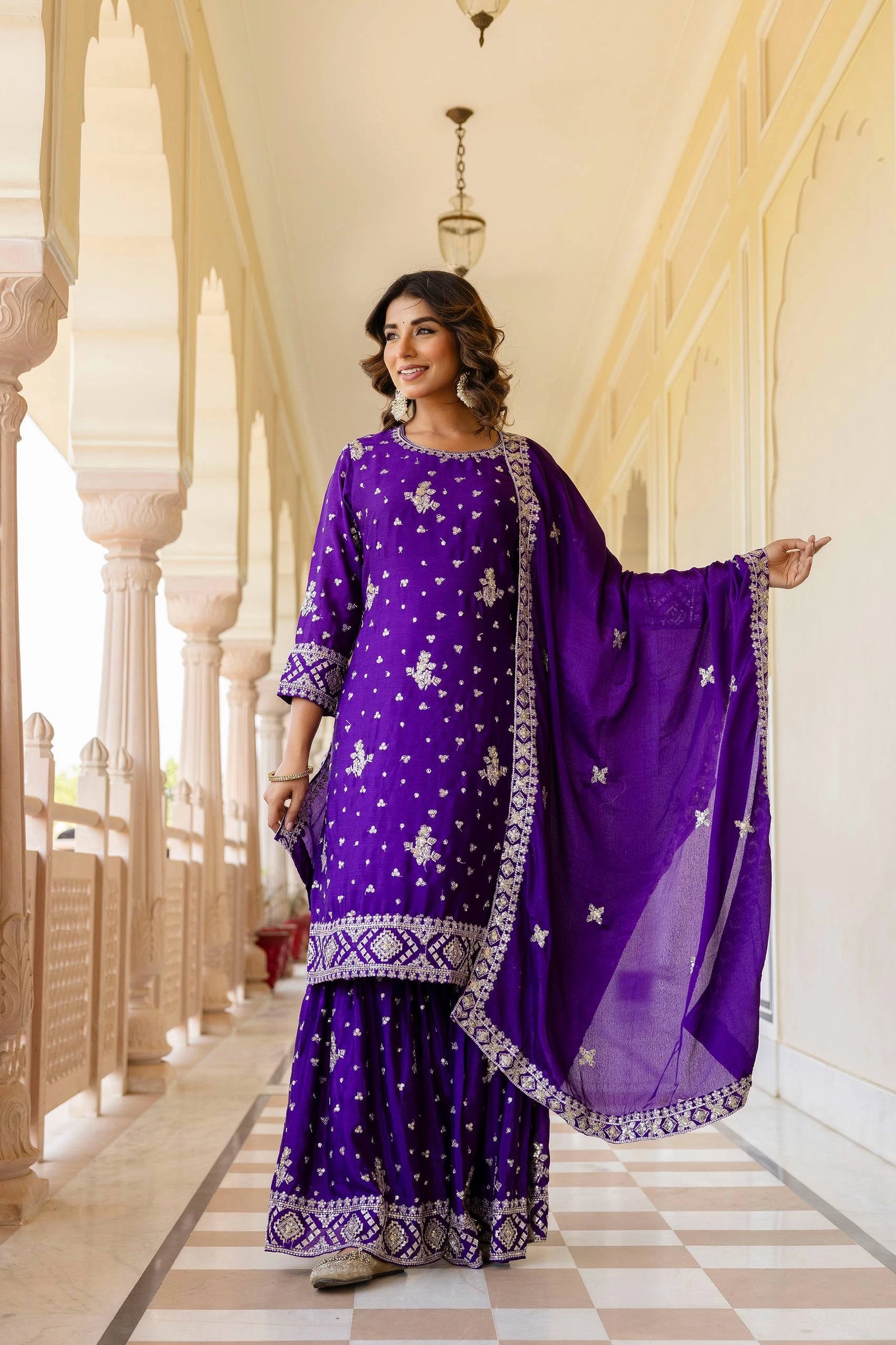 Woman in a purple traditional outfit standing in an elegant hallway.