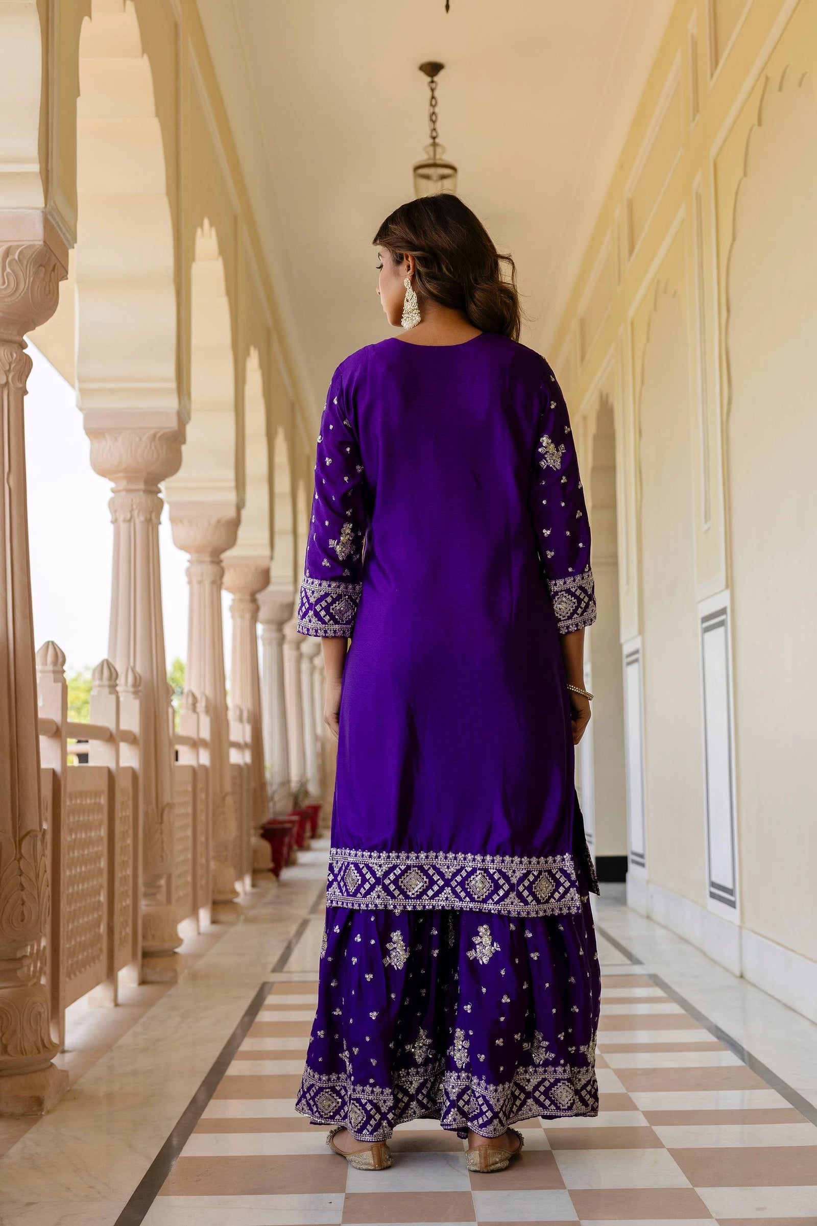 Woman in a purple traditional outfit walking along a corridor with columns.