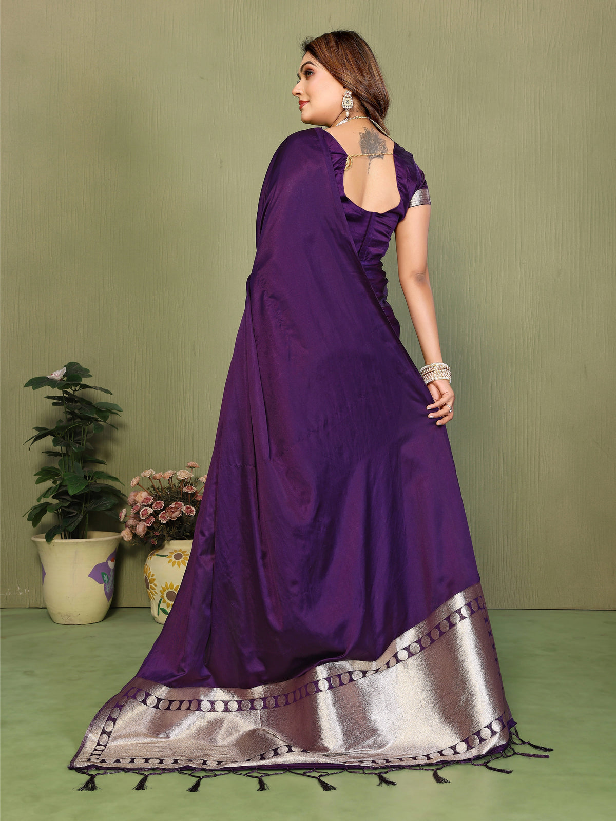Woman wearing a purple saree with silver border on a green background
