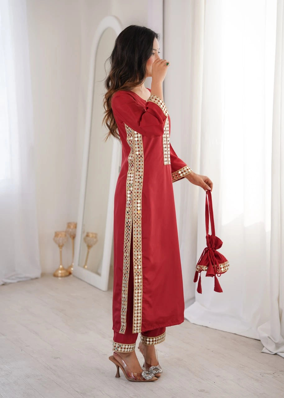 Woman in a red traditional outfit with gold embroidery holding a matching bag in a bright room.