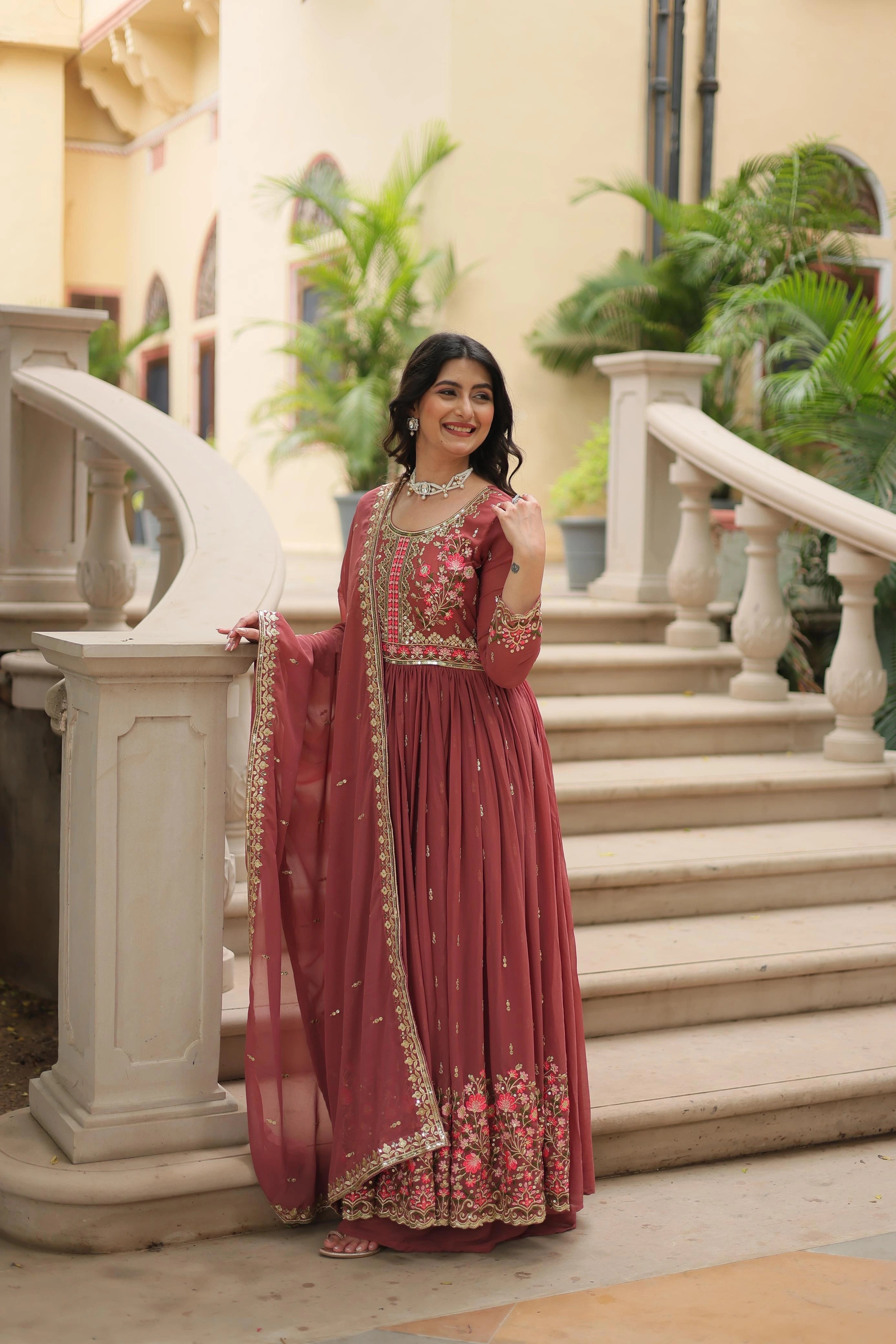 Woman in a red traditional outfit standing on steps with greenery in the background