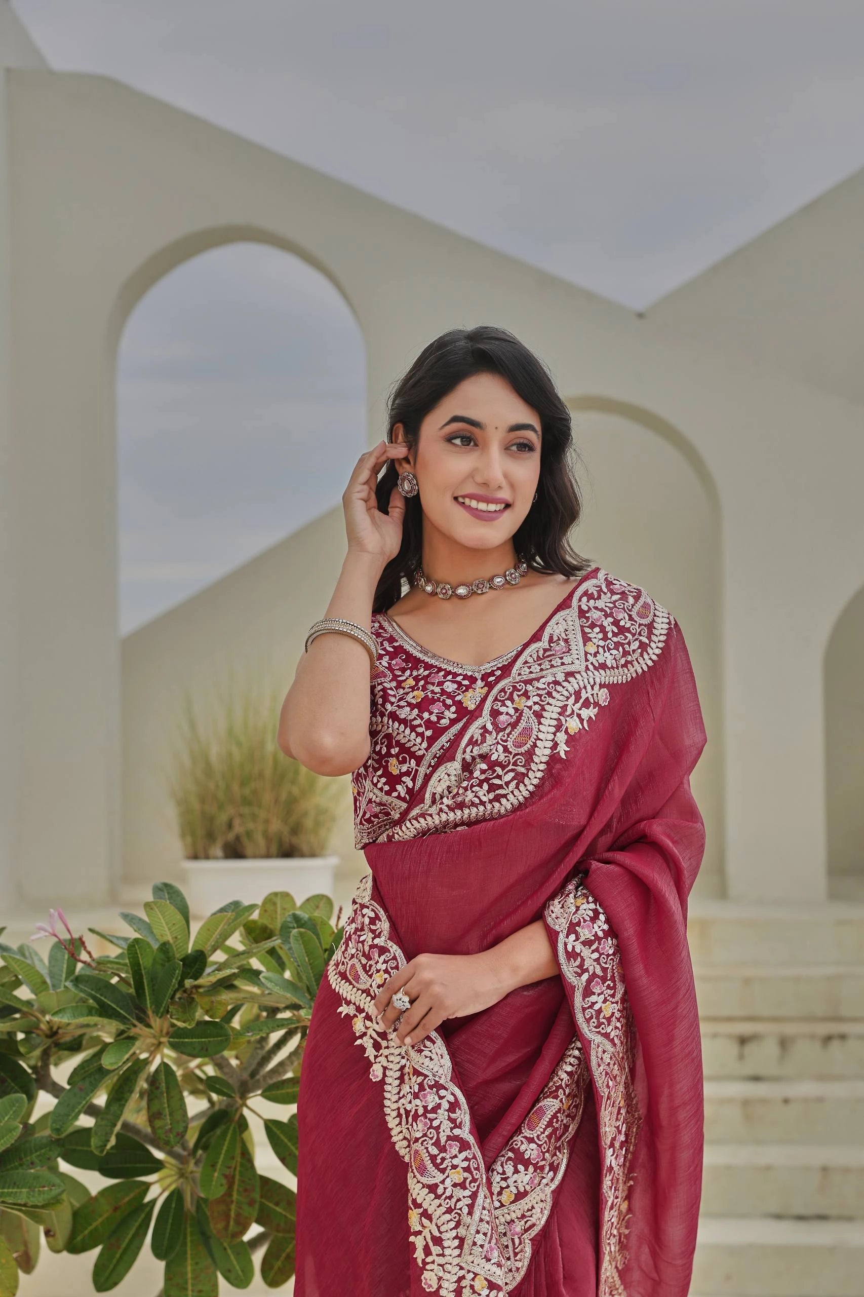 Woman in a maroon saree with white embroidery standing outdoors.