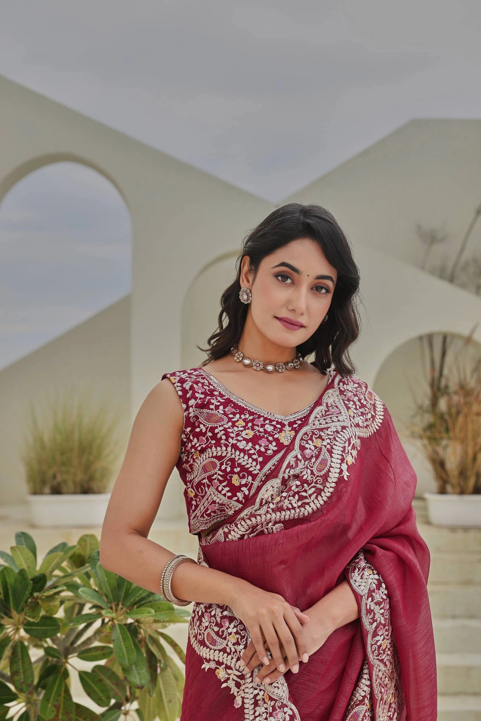 Woman in a maroon saree with white patterns standing outdoors.