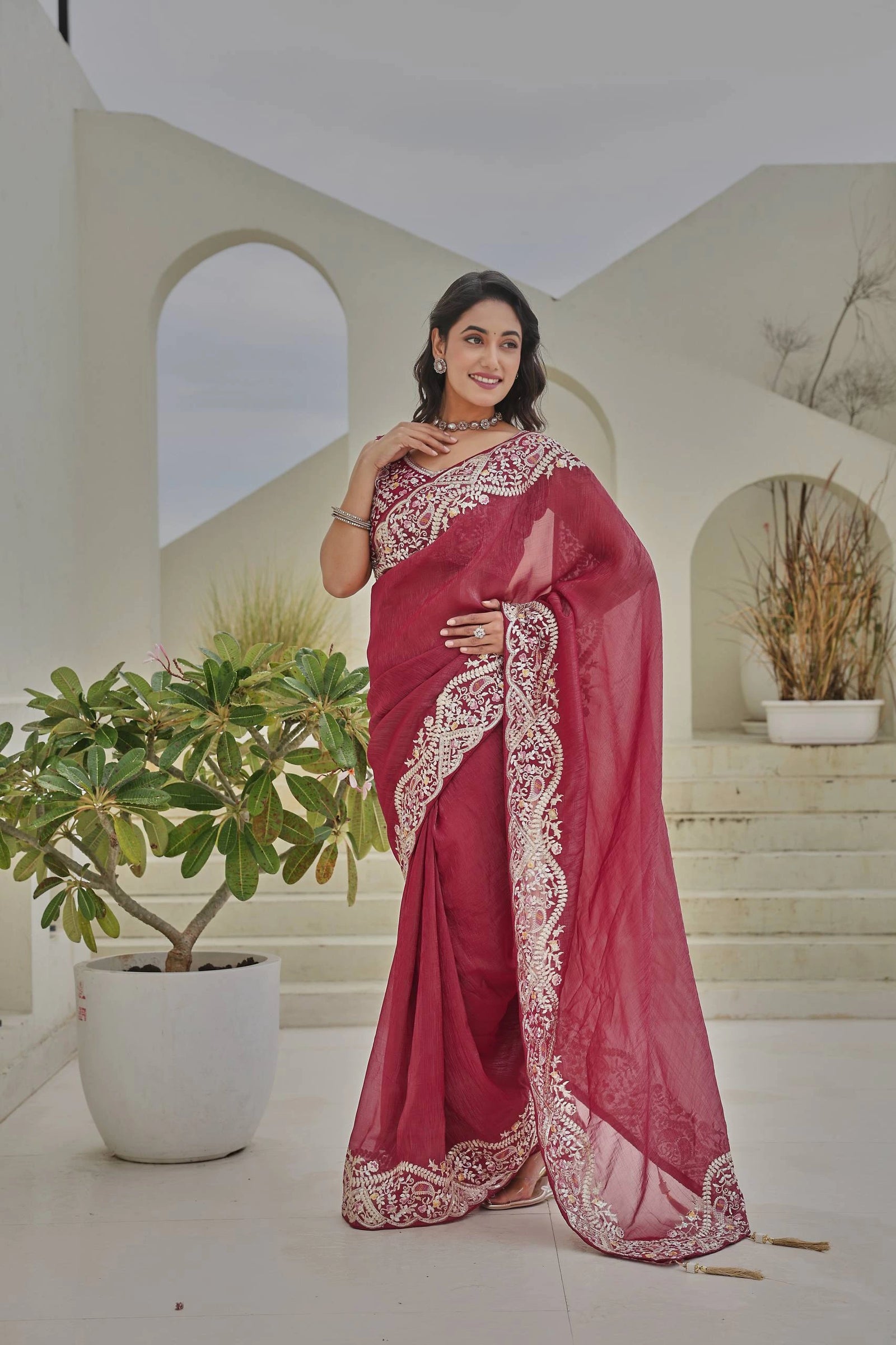 Woman in a red saree with white embroidery standing in a decorative indoor setting.