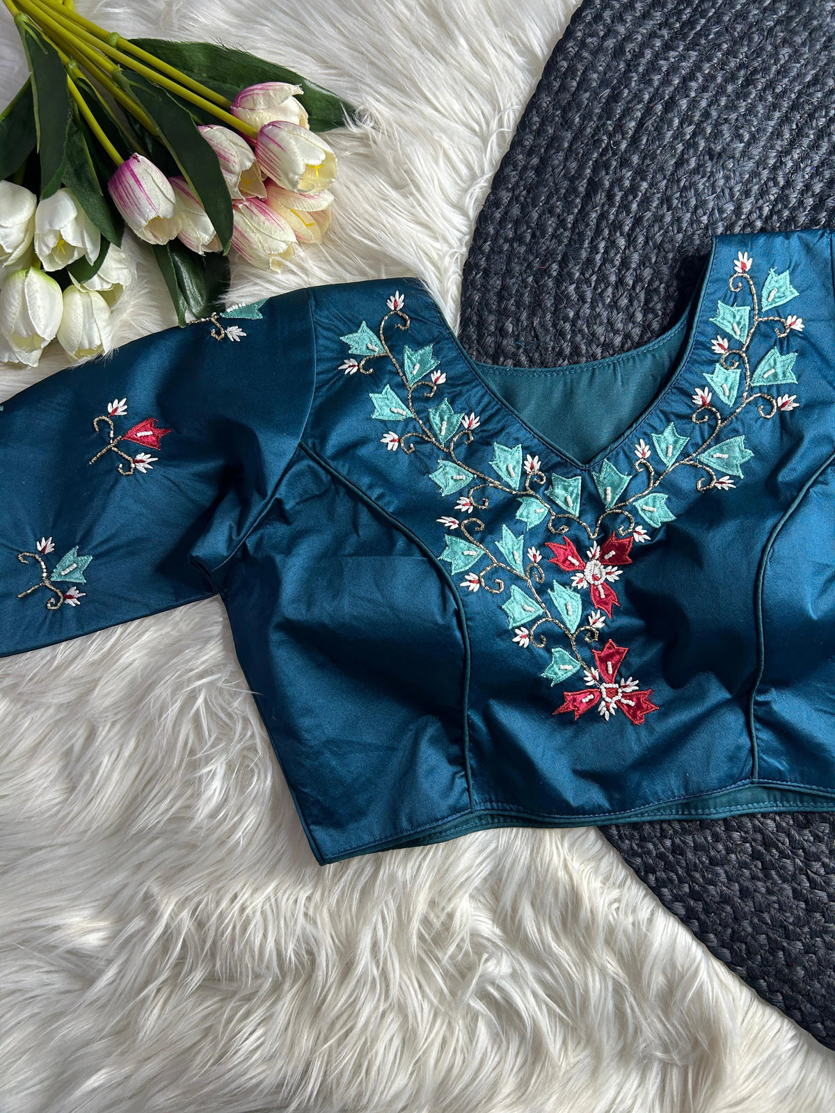 Blue embroidered blouse with floral patterns on a white textured surface with tulips.