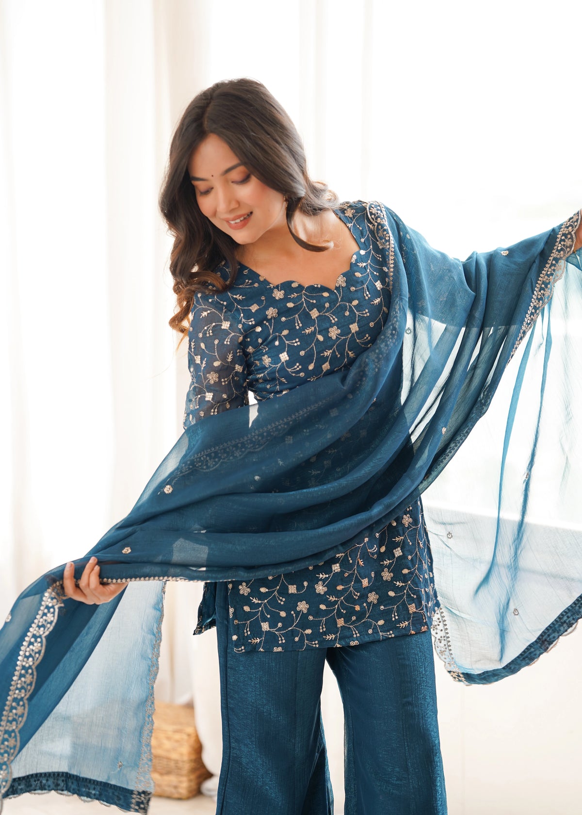Woman wearing a blue traditional outfit with a sheer dupatta in a bright room.