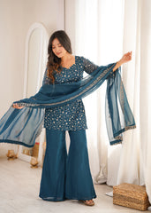 Woman in a blue traditional outfit holding a matching scarf in a bright room.