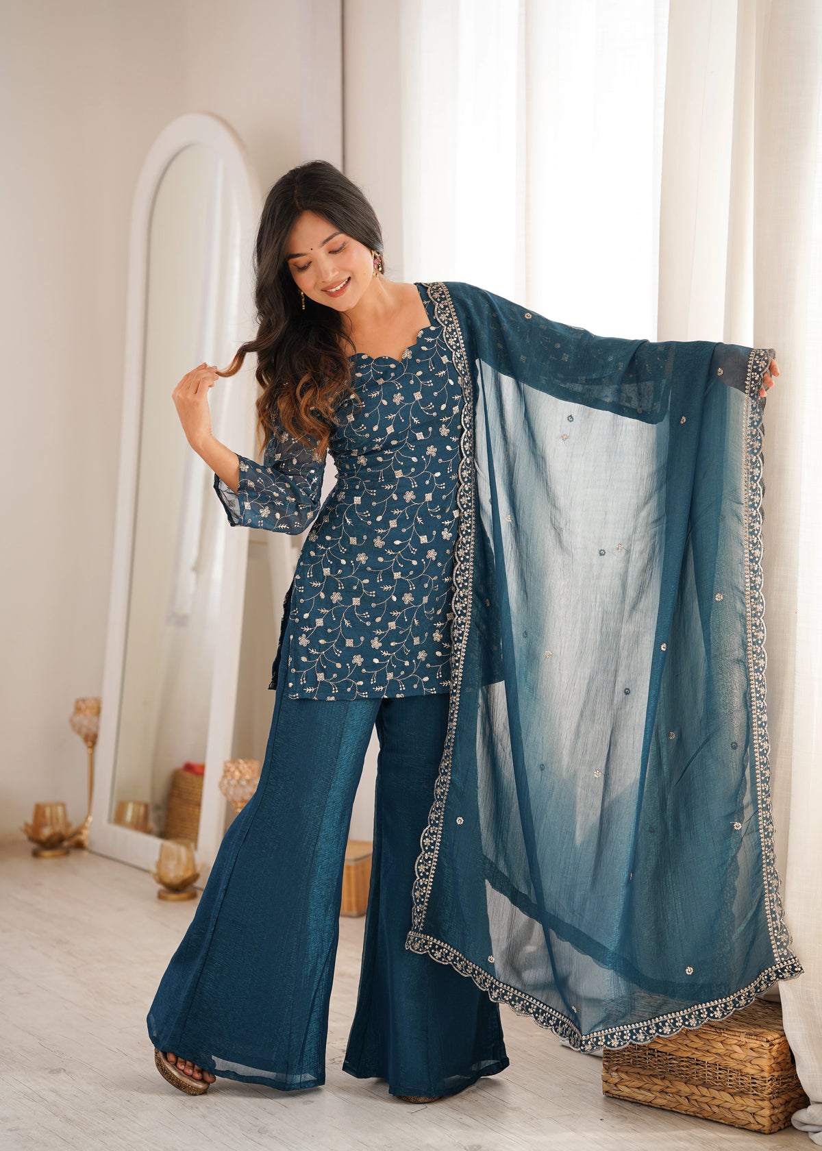 Woman holding a blue traditional outfit with a matching dupatta in a well-lit room.