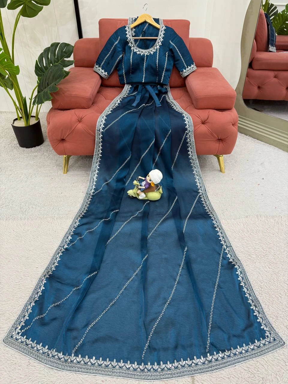 Blue saree with silver border on a hanger against a living room background