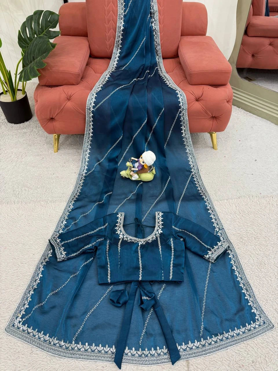Blue embroidered garment on a white surface with a red couch in the background