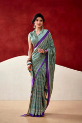 Woman wearing a green and purple saree against a red and beige background