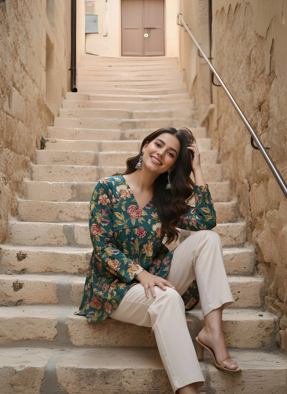 Woman sitting on stone steps in an alleyway wearing a floral top and beige pants.