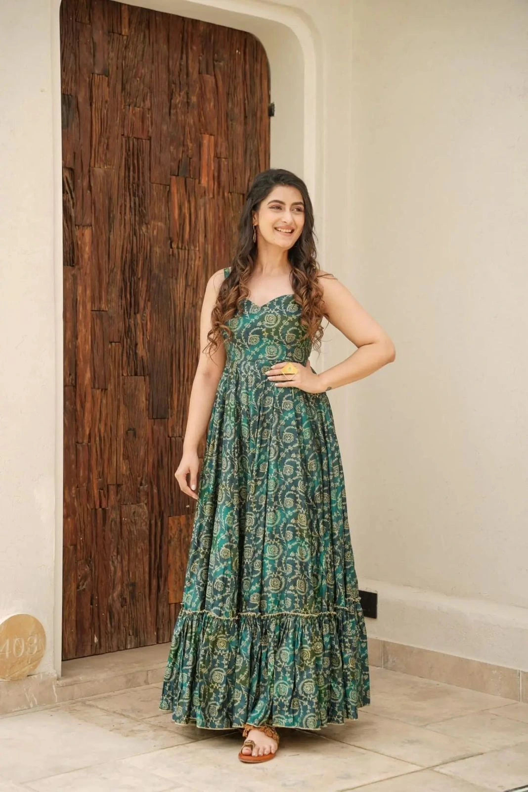 Woman wearing a green floral dress standing in front of a wooden door.