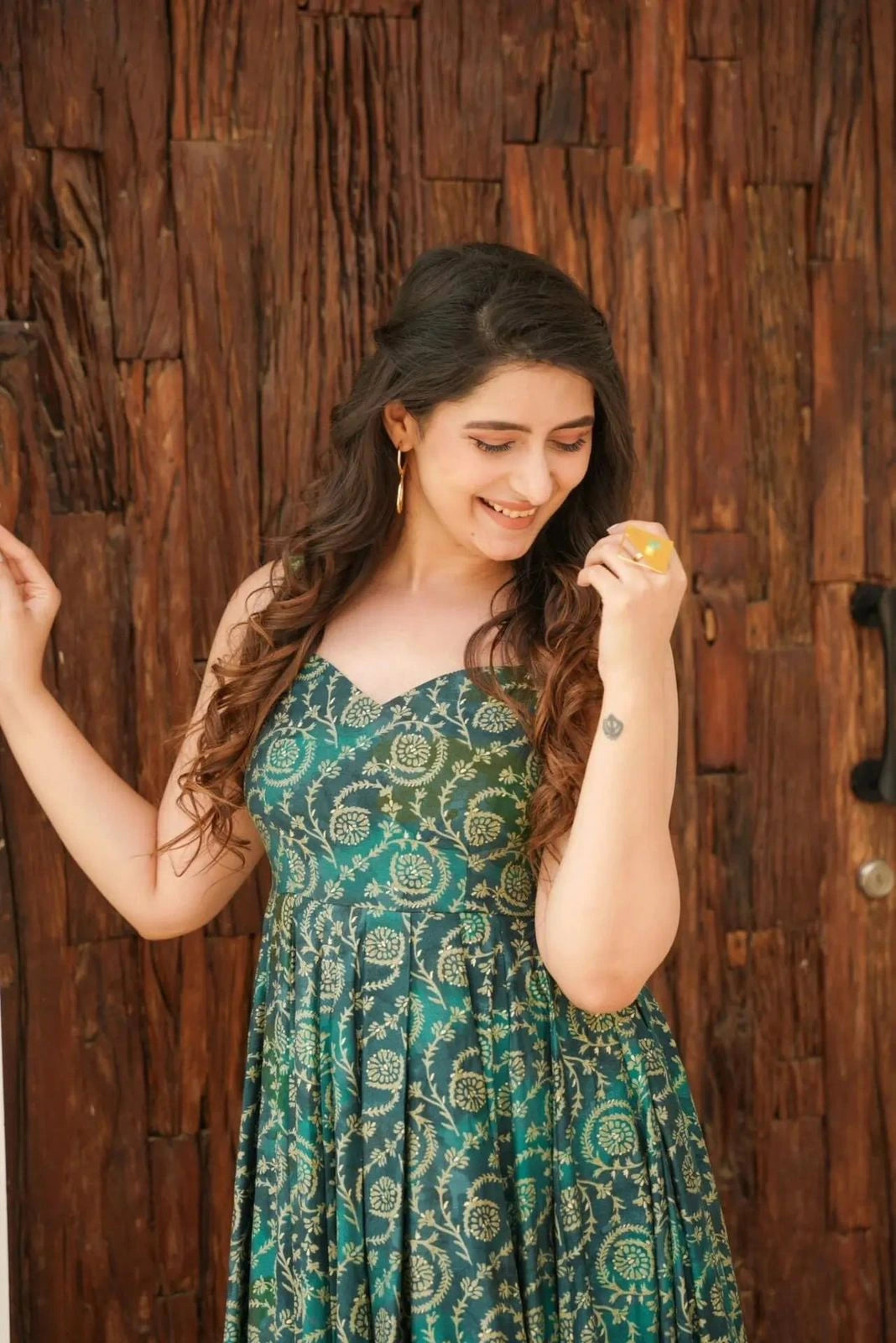 Woman in a green patterned dress holding a small object against a wooden background