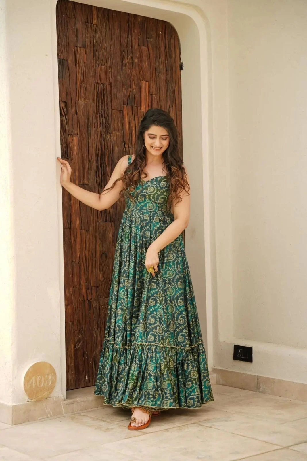 Woman in a green patterned dress standing in a doorway.