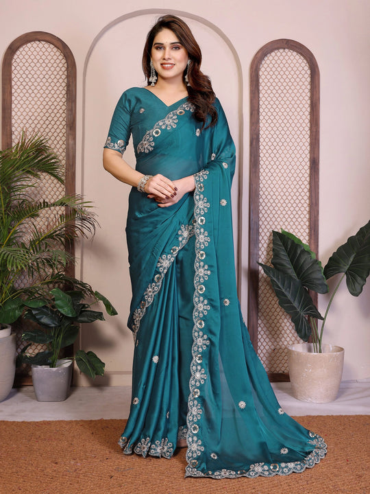 Woman wearing a teal saree with floral patterns in an indoor setting.