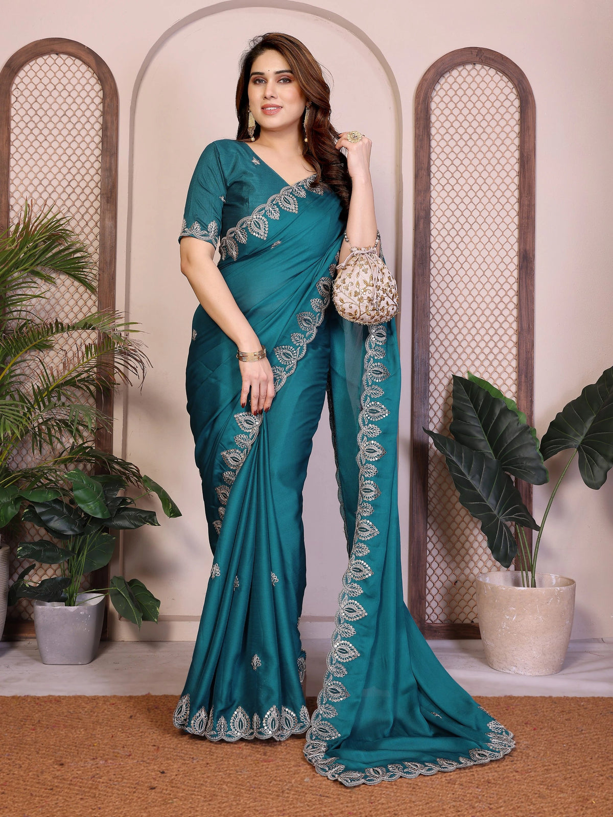 Woman wearing a teal saree with silver embroidery in an indoor setting with plants.