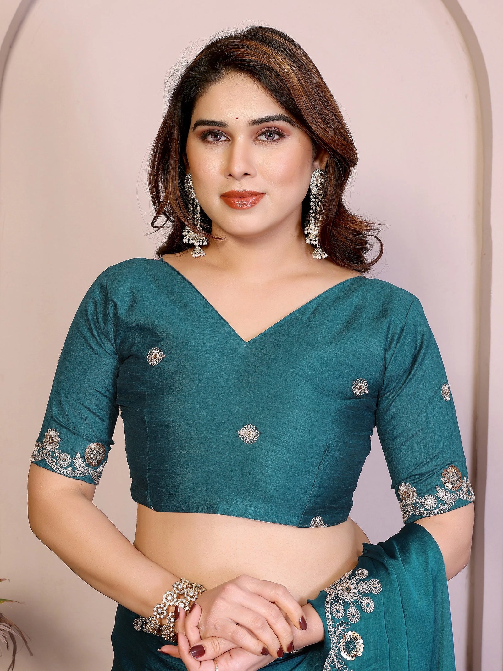 Woman wearing a teal saree with silver embellishments against a beige background