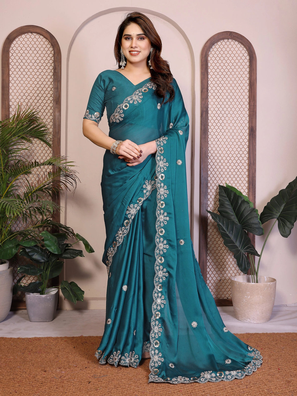 Woman wearing a teal saree with floral patterns in an indoor setting.