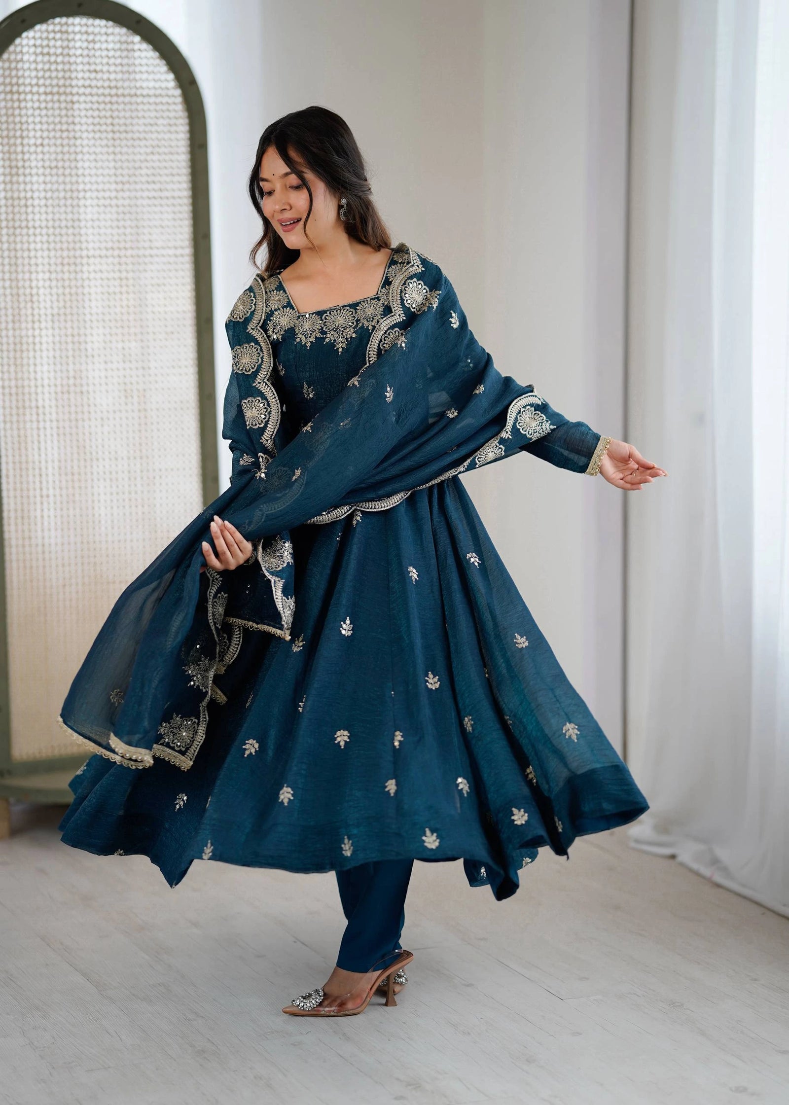 Woman in a blue traditional outfit with white patterns standing indoors.